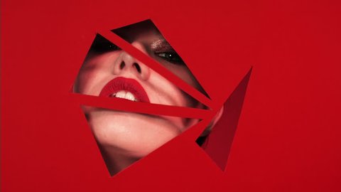 Face of girl with beautiful bright make-up appears in triangular holes of red paper background. 