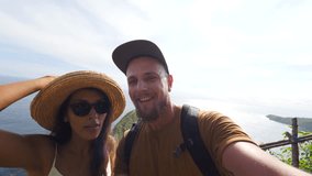Young Mixed Race Tourist Couple Making Funny Selfie Video Chat with Amazing Kelingking Beach on Background. Nusa Penida, Indonesia. 4K.