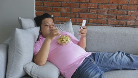Picture of greedy person feels hungry and eat snack while leaning on the couch using smart phone