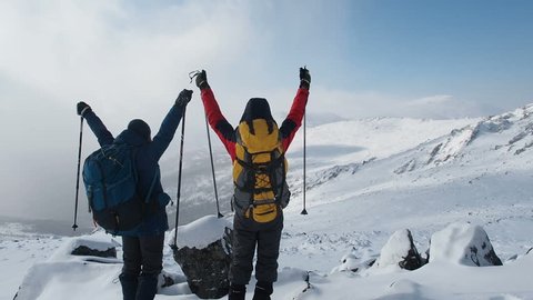 Young Active Successful People Raising Hands On Mountain Top. Hikers Couple with arms raised on top of mountain. Hikers lifting arms up enjoying nature vacation travel adventure. Winter Snow Extreme 