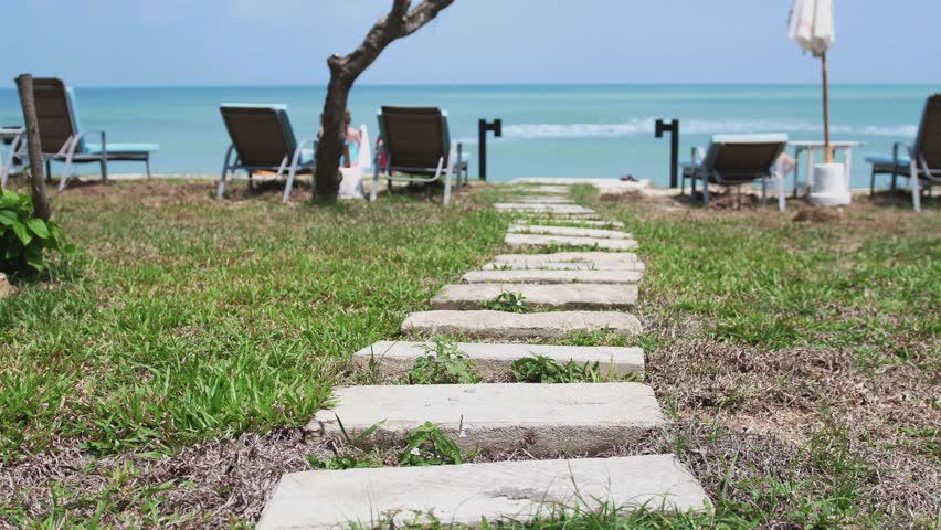 Wonderful path from stones to the ocean shore with umbrellas and sunbeds in slow motion. Thailand. 3840x2160