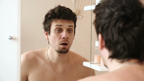 Tired man who has just woken looks at its reflection in the mirror, yawns and hits themselves on cheeks, to wake up.