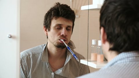 Tortured sleepy only waking man in front of the mirror with a toothbrush in his mouth.