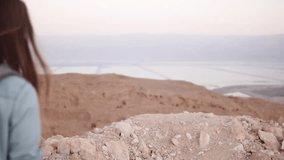 Woman takes photos of montain scenery. Slow motion. Casual traveler girl with backpack using smartphone. Israel Dead Sea