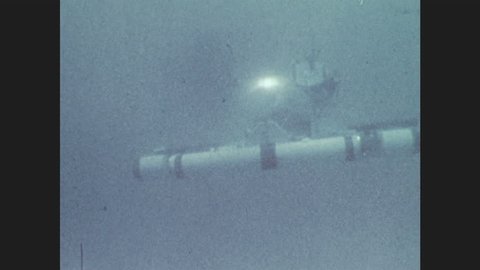 1970s: A submersible moves underwater. Two men sit inside a submersible underwater. Panoramic view of landscape with a river.