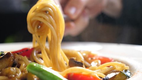 Italian cuisine in restaurant eating spaghetti pasta with vegetables with a fork closeup