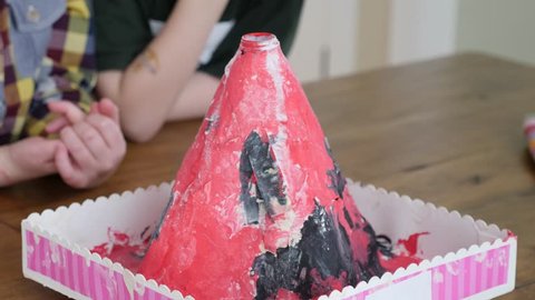 Cute boys do a volcano science experiment at the table in their house