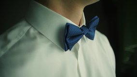 Man adjusting bow tie. Clip. Close-up of young man in white shirt adjusting his bowtie while standing