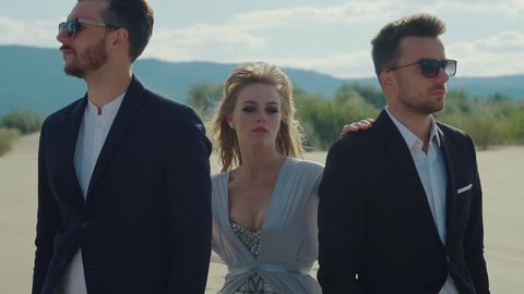 Blonde is standing between two boyfriends in a desert. Strange relationships of woman with two man, abstract shot on a beach