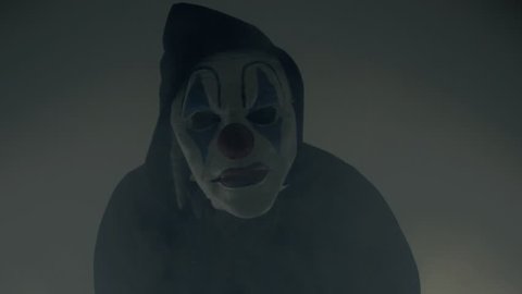 A scary clown in the dark, surrounded by smoke/fog