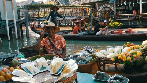 PATTAYA, THAILAND - December 18, 2017: The seller in a colorful shirt and a straw hat sells exotic Thai fruits on a boat