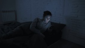 low light video lateral panning shot of young attractive hispanic woman on her 30s lying in bed late night using mobile phone looking tired in internet social media lifestyle addiction