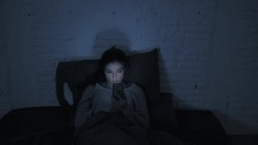 low light video frontal shot of young attractive hispanic woman on her 30s lying in bed late night using mobile phone tired and sleepless in internet social media addiction concept