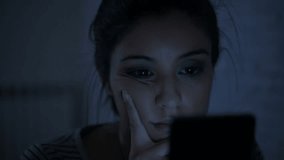 low light video close up head shot of young attractive hispanic woman on her 30s late at night using mobile phone looking tired and bored in internet social media addiction