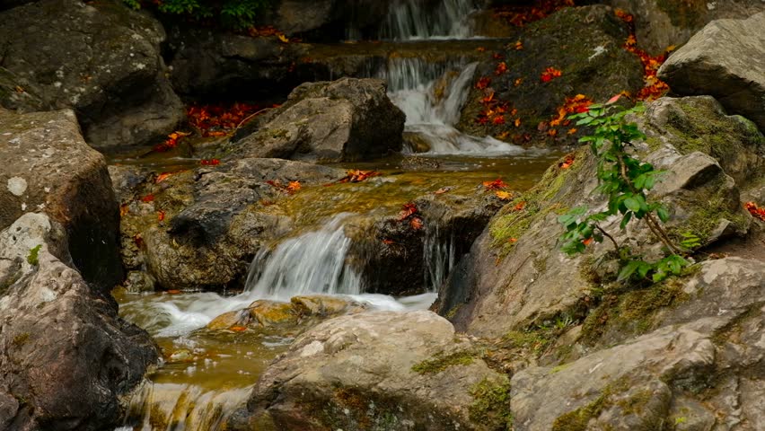 Cascade of boulders in mountine creek with red fallen leaves