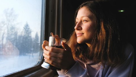 Beautiful caucasian girl drinks tea and looks out the window on the train and smiles, 4k.