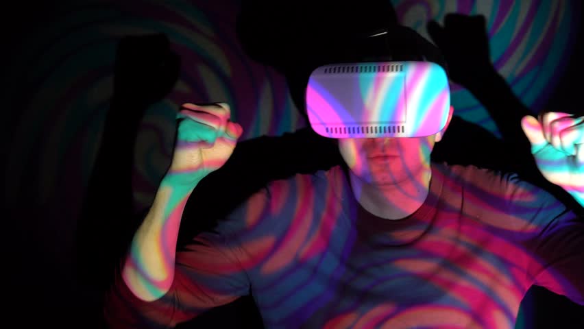 Young man in virtual reality glasses doing victory dance about successful achievement on bright spotlight background Royalty-Free Stock Footage #1008165556
