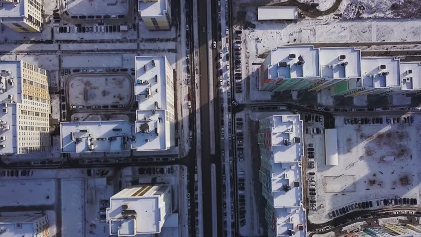 Aerial view snow-covered road with cars in winter. Clip. Aerial view on city in winter day. City panorama with straight road covered with snow from a bird eye view. Winter city streets from a bird eye