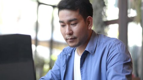 Young handsome businessman (student) in a blue shirt, at the table working with a laptop,
