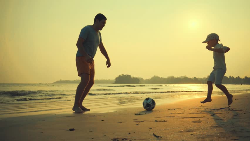 Father and son playing together with ball in football on the beach under sunset background Royalty-Free Stock Footage #1008171754
