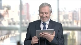 Happy senior businessman with pc tablet. Smiling elderly businessman looking at digital tablet and waving with hand, window city background. Video conference concept.