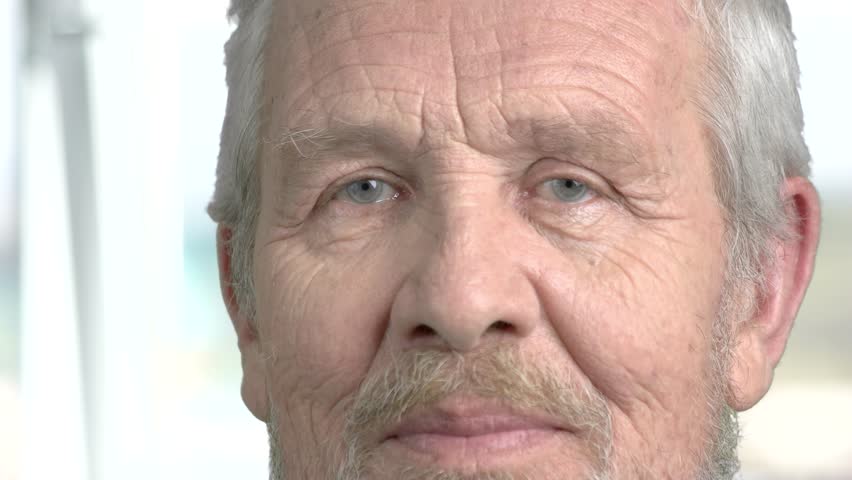Face of confused elderly man close up. Smiling wrinkled face of senior man close up. Human facial expression.
