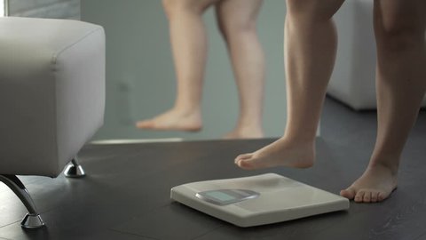 Overweight female hesitating before stepping on scales to check weight, fear