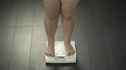 Healthy diet, chubby female stepping on scales to check weight, body control