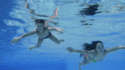 Boy and girl dive in swimming pool together, underwater slow motion
