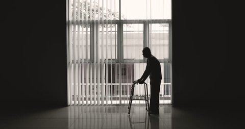 Silhouette of elderly man walking near the window using a walker. Shot in 4k resolution