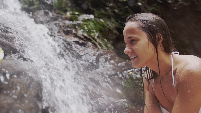 Cheerful girl washing her face in a stream of water in a natural waterfall. slow motion. 1920x1080
