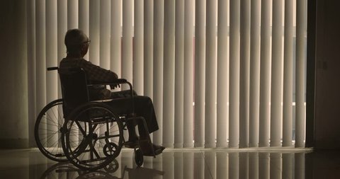 Silhouette of lonely old man sitting on wheelchair while looking at the window with curtain at home. Shot in 4k resolution