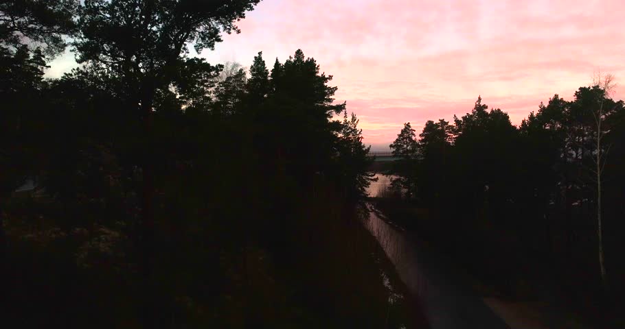 Sunset at a bridge, Cinema 4k aerial rising view over trees revealing a red sky above lovo bridge, on a sunny winter evening dawn, in Varsinais-suomi, finnish archipelago, Finland