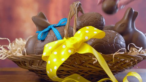 Happy Easter hamper of chocolate eggs and bunny rabbits in large basket with silk tulips on dark wood table, stacking eggs.