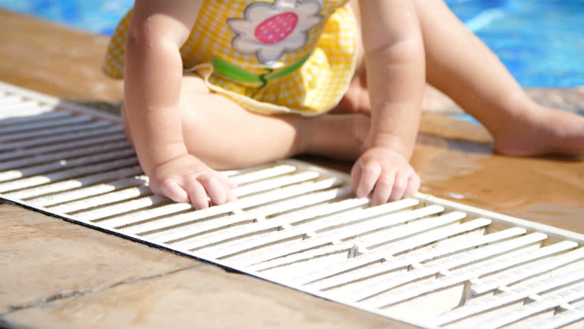 on the edge, near the pool sits a one-year-old baby, child, barefoot, in a swimsuit.