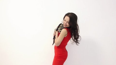 young happy girl in red dress is dancing with a ferret on white wall background