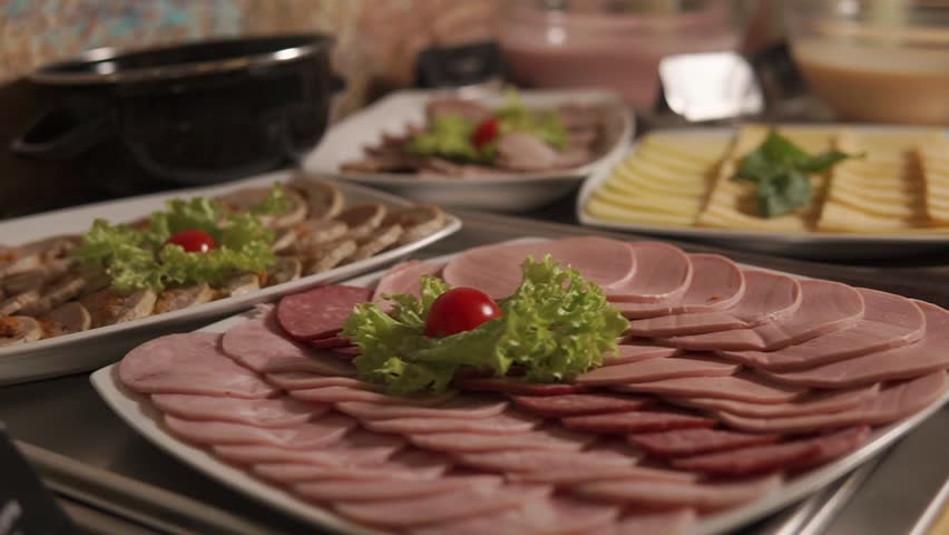 Cut sausages and meat with cheese are in a tableware on a table. Preparing for servicing a banquet at the restaurant