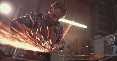 Blacksmith cutting metal using angle grinder while working in industrial workshop