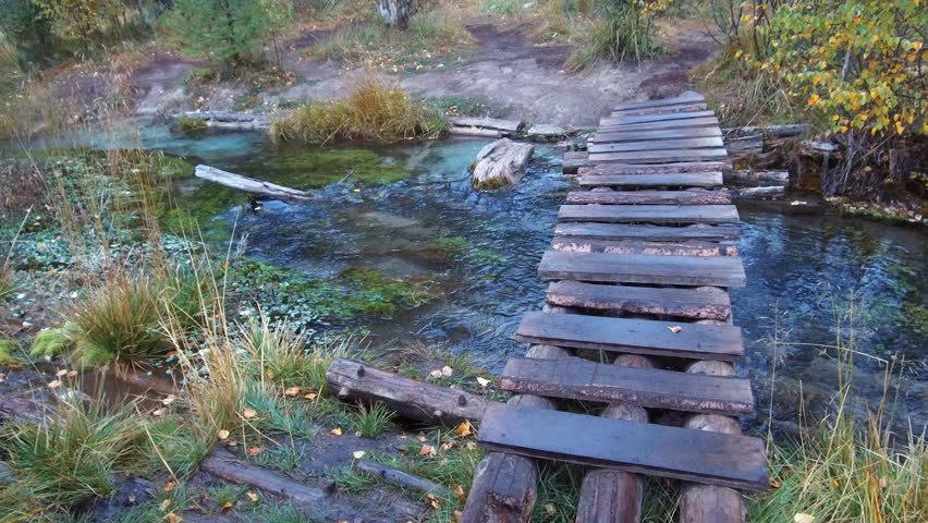 Crossing small wooden bridge over forest creek near Blue Geyser lake in Altai mountains in rainy Autumn day
