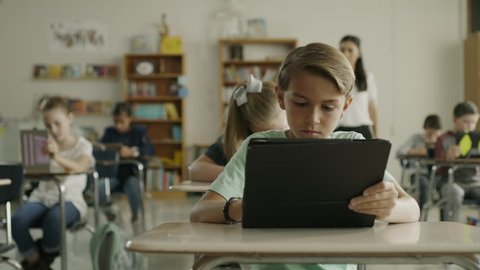 Panning shot of teacher assisting children in classroom reading digital tablets / Provo, Utah, United States