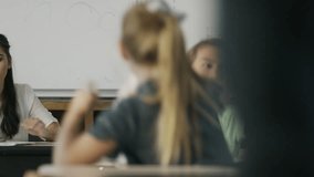 Frustrated teacher sitting at desk watching children in chaotic classroom / Provo, Utah, United States