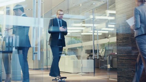 Stylish Suited Businessman Uses Smartphone Rides Skateboard Through the Corporate Building Hallway. Stylish Glass and Concrete Building with Multicultural Crowd of Business People.  RED EPIC-W 8K.