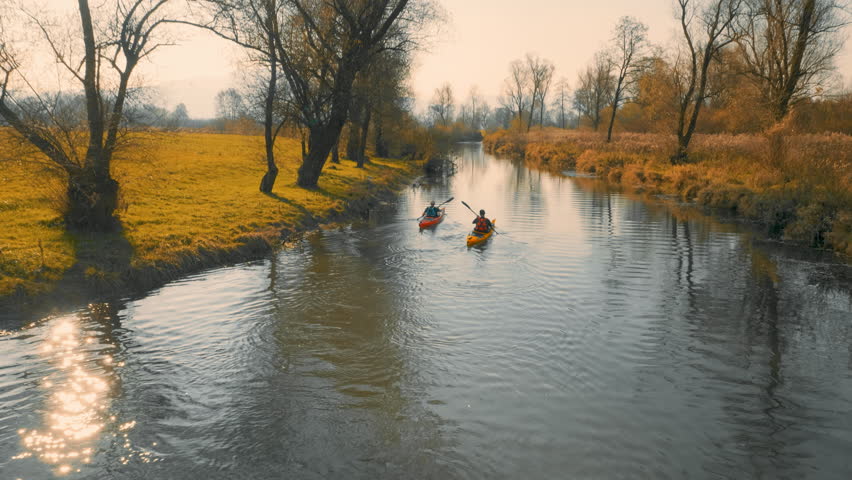 Aerial tracking shot of kayakers paddling up the river in in amazing landscape on a beautiful autumn sunny day.