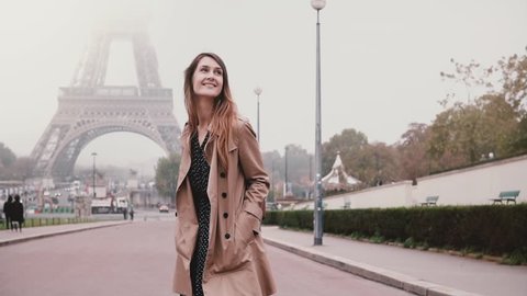 Young attractive woman walking near Eiffel tower in Paris, France. Happy girl looking around and smiling. Slow motion.