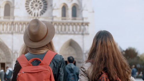 Back view of two traveling woman with backpack walking near the Notre Dame, famous cathedral in Paris, France.