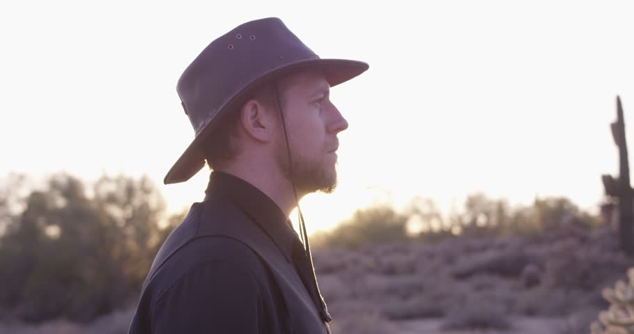 American Cowboy turns around in desert to reveal gorgeous orange sun - slow motion