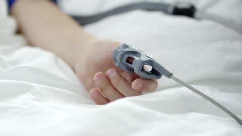 Arm of child lying in hospital bed with pulse oximeter on thumb