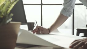 Large white sheet with drawings on the table in front of a male architect. The man-architect with stylish accessories - rings, watches, - makes notes on the drawing. Close-up, only hands. - Powered by Shutterstock - Get 15% off with code: PIKWIZARD15