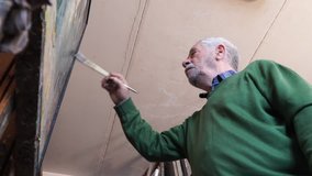 The old painter paints his own portrait with oil paint. 4K Video. 