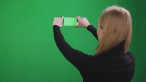 Girl takes video on smartphone, green background.
